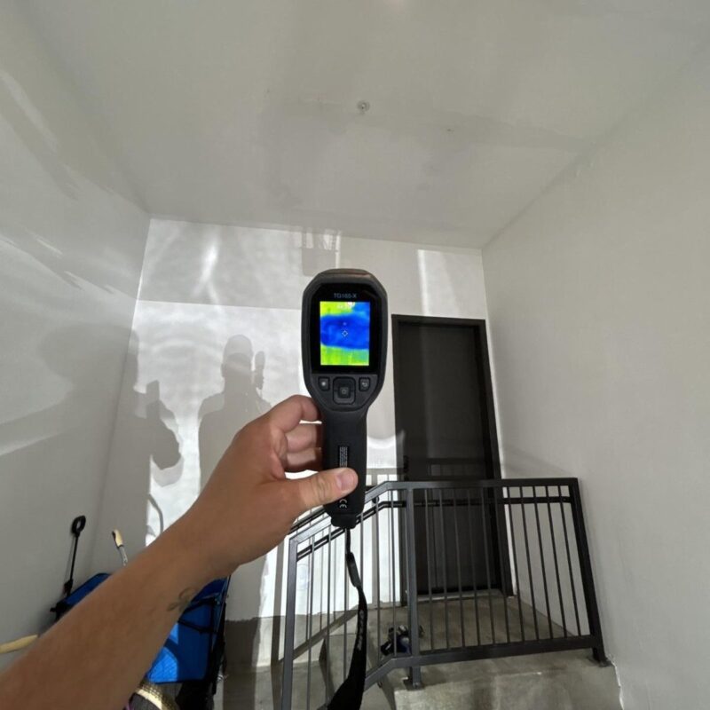 Technician using a thermal imaging camera to check a stairwell ceiling for hidden moisture