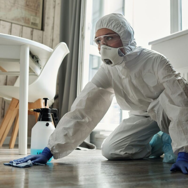 Technician in full PPE disinfecting a floor during bio-hazard cleanup