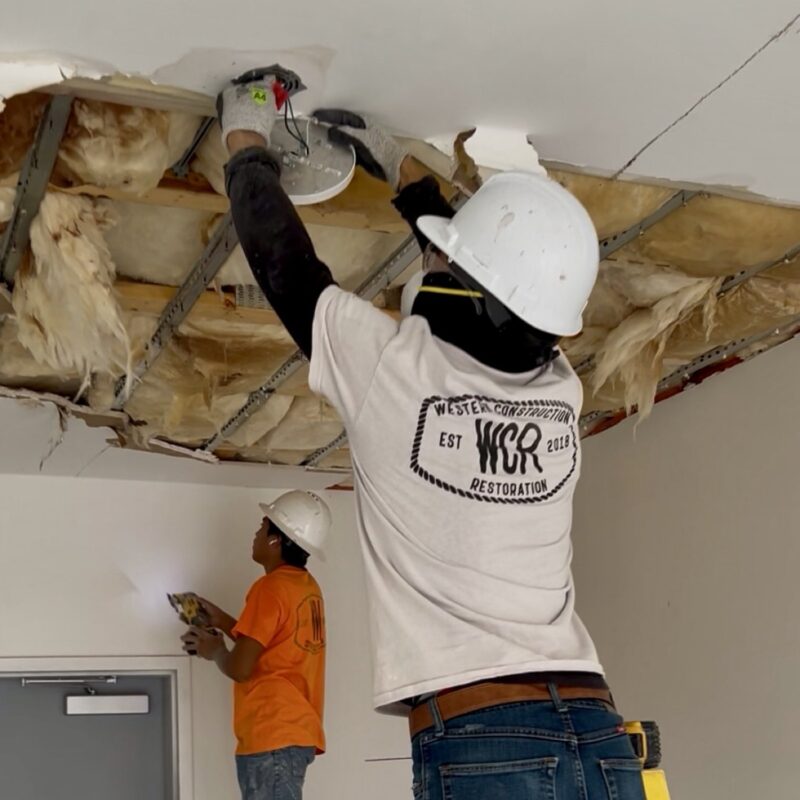 Western Construction & Restoration crew in hard hats removing water-damaged ceiling drywall and insulation during remediation