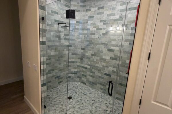 Frameless glass corner shower with green marble subway tile and hex mosaic floor, bathroom remodel by Western Construction & Restoration