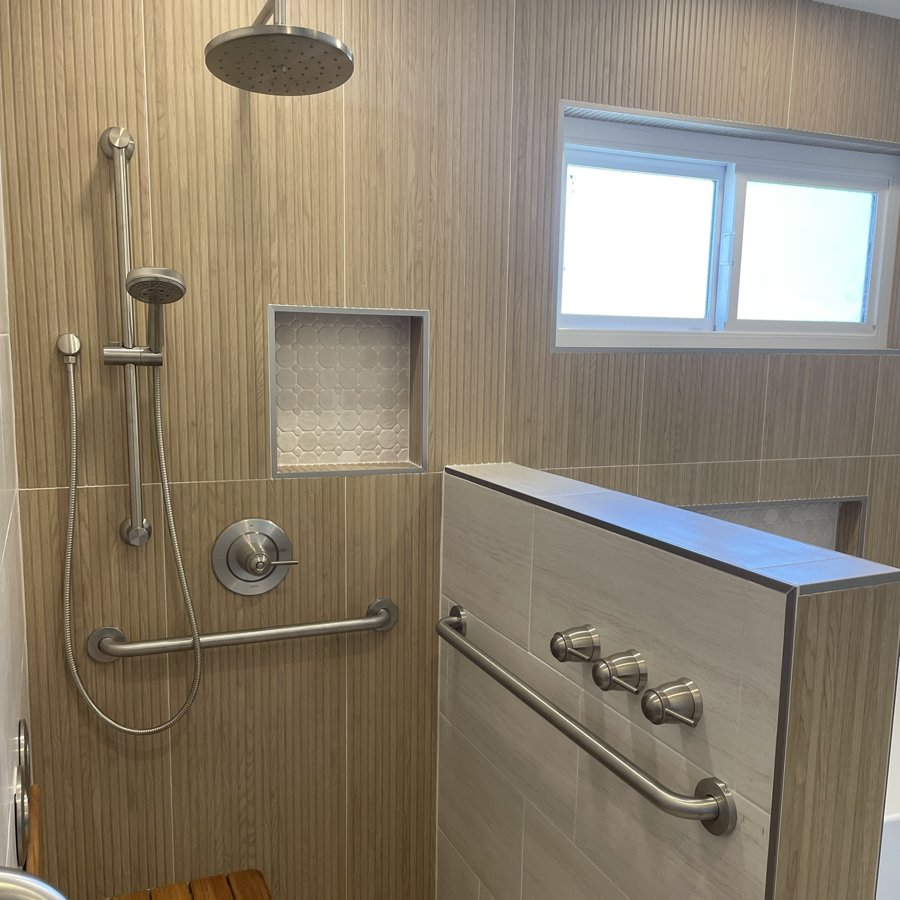 Remodeled walk-in shower with wood-look tile, grab bars and teak bench by Western Construction & Restoration