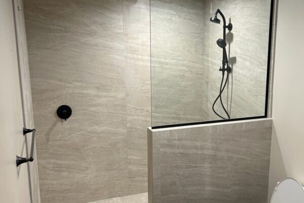 Walk-in shower with large-format stone-look tile, glass panel and matte black fixtures, bathroom remodel by Western Construction & Restoration